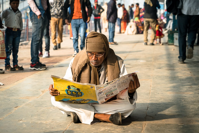 Man reading newspaper on Indian train platform. 