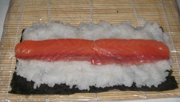 вареный рис с ломтиком филе красной рыбы на листе нори на деревянном коврике, застеленном пакетом